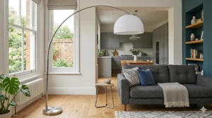 A sleek chrome arc floor lamp standing next to a grey sofa in a bright, open-plan British lounge that flows into a modern grey kitchen.