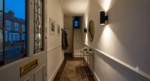 Sleek matt black up and down wall lights indoor illuminating a narrow terraced house hallway.