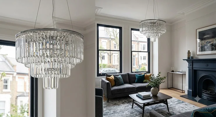 A modern crystal chandelier hanging in a contemporary London living room with high ceilings.
