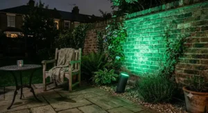 Waterproof outdoor colour changing uplighter illuminating a brick garden wall with vibrant green light.