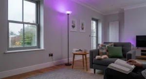 A smart colour-changing LED uplighter casting soft purple mood lighting against a neutral living room wall.